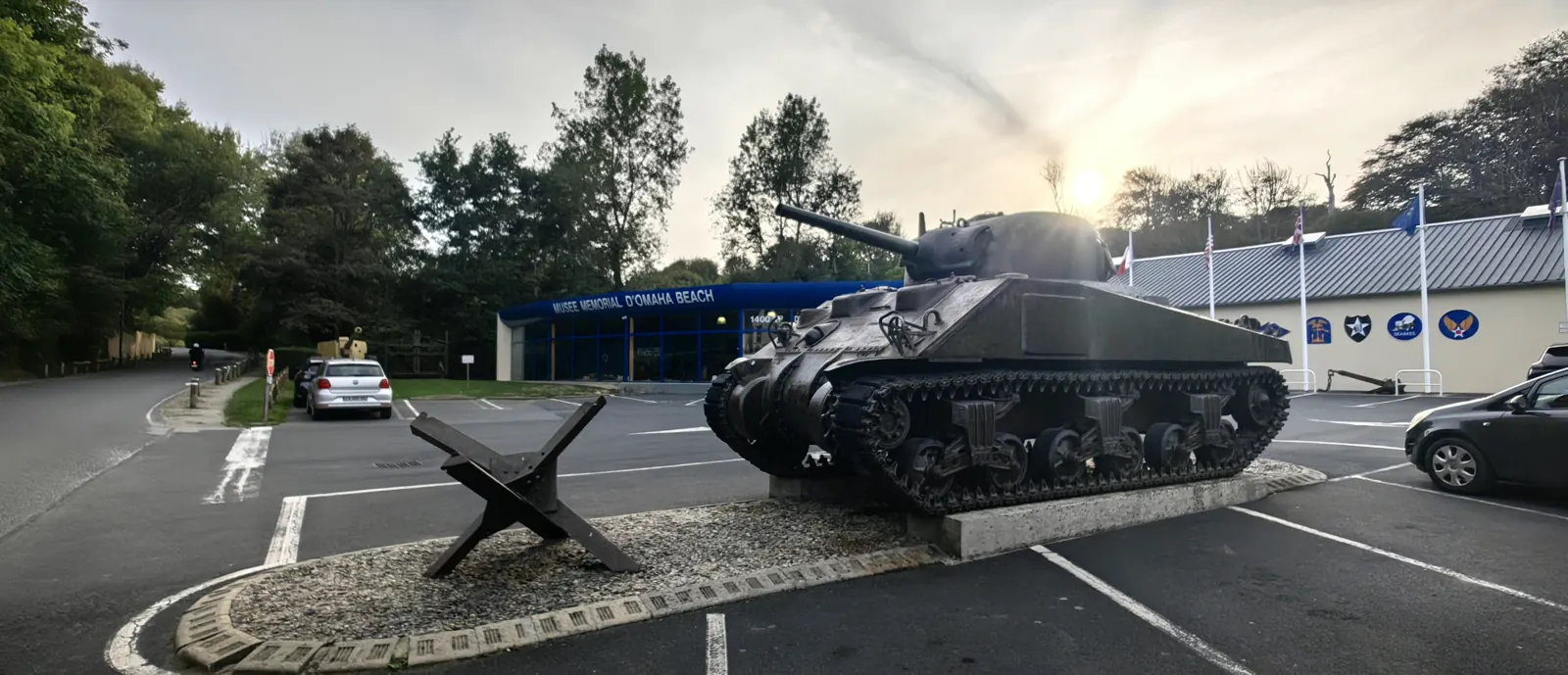 Sherman tank on its plinth with a Czech hedgehog beach obstacle beside it in front of the Omaha Beach Memorial Museum, Saint-Laurent-sur-Mer, in evening sun