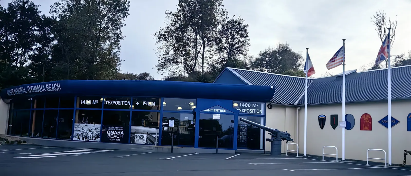 Entrance of the Musée Mémorial d'Omaha Beach in Saint-Laurent-sur-Mer: blue frontage, a gun in front and signs announcing 1400 m² of exhibition and a film
