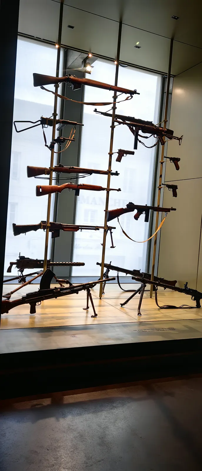 Rack of Second World War rifles, submachine guns and machine guns in front of a bay window at the Overlord Museum, a D-Day museum in Normandy